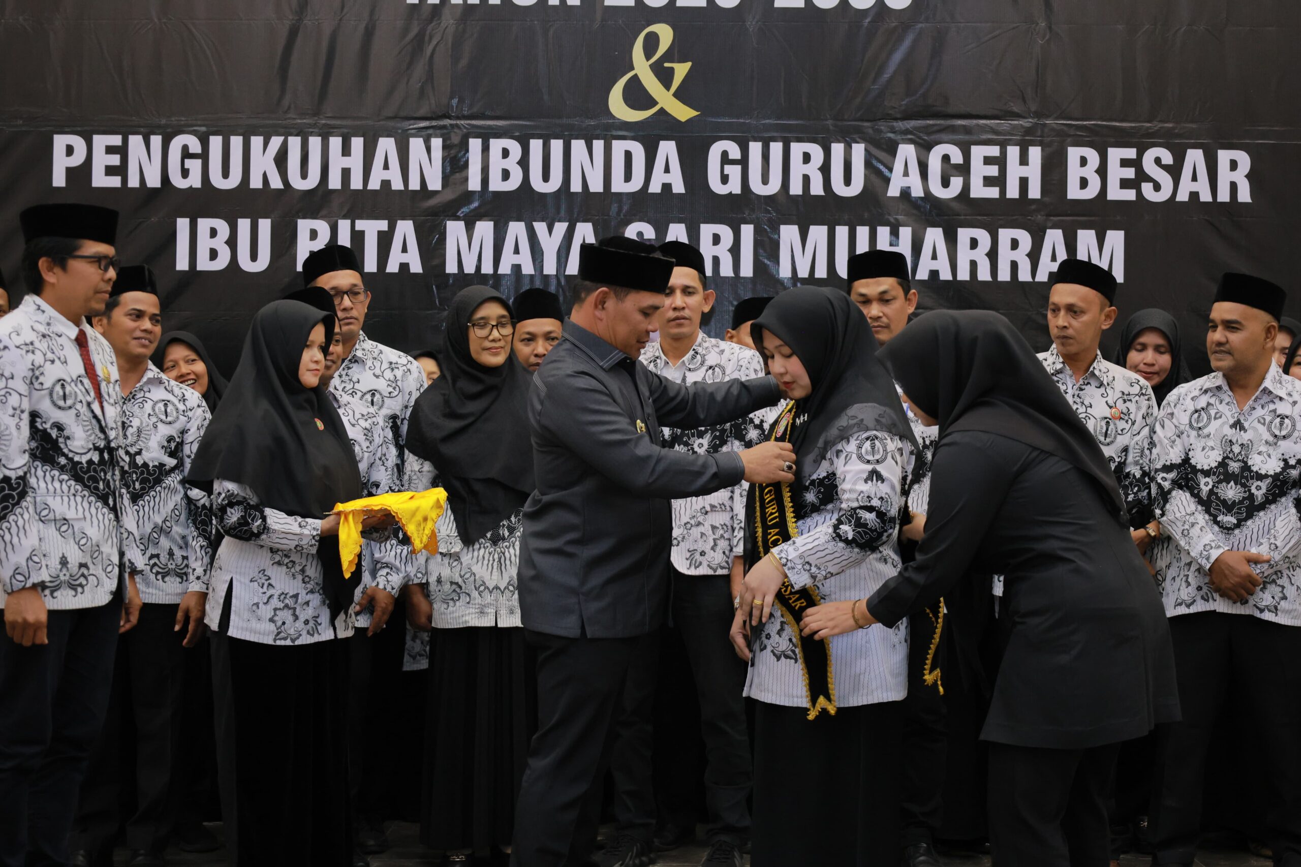 Bupati Aceh Besar H. Muharram Idris memakai slempang pada Bunda Guru Aceh Besar Hj. Rita Maysari di Orion Hall, Kecamatan Darul Imarah, Jumat (6/2/2026) malam. FOTO/MC ACEH BESAR