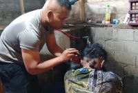 Aipda Candra Sugara, SH saat memangkas rambut pasien penderita gangguan saraf, Minggu (26/7/2026), di wilayah Kecamatan Bandar.(Dok: Rahmat Ramadhan)