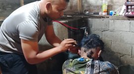 Aipda Candra Sugara, SH saat memangkas rambut pasien penderita gangguan saraf, Minggu (26/7/2026), di wilayah Kecamatan Bandar.(Dok: Rahmat Ramadhan)
